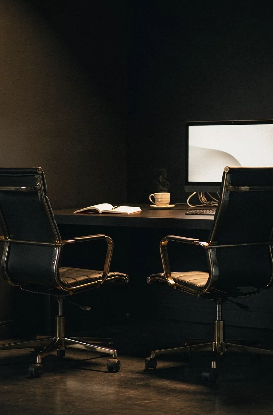 Two office chairs facing a desk with an open notebook and glowing monitor, representing the AI interviewing you before it writes