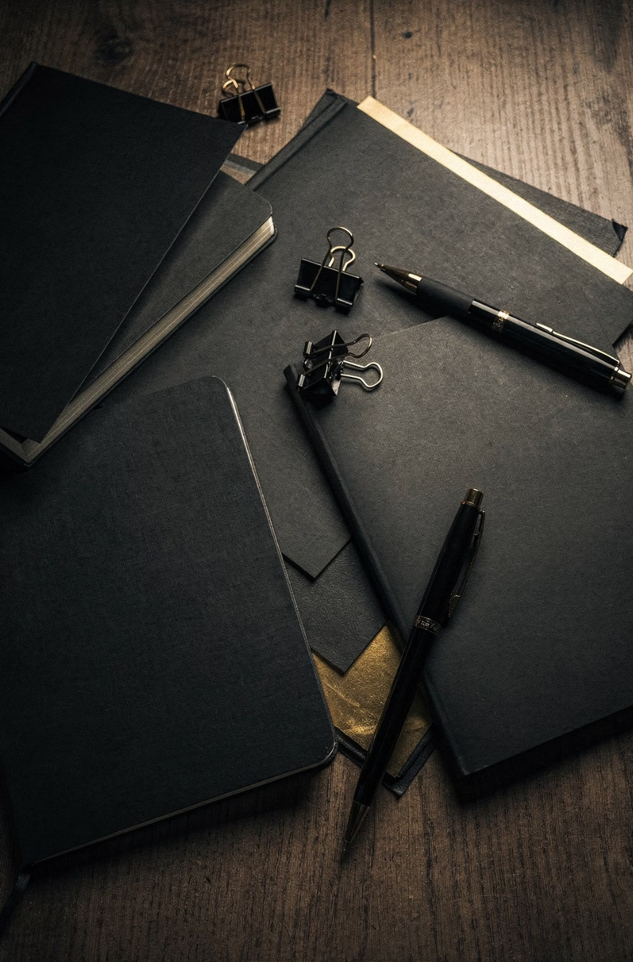 Black notebooks and pens scattered on a wooden desk, the analog version of scattered notes