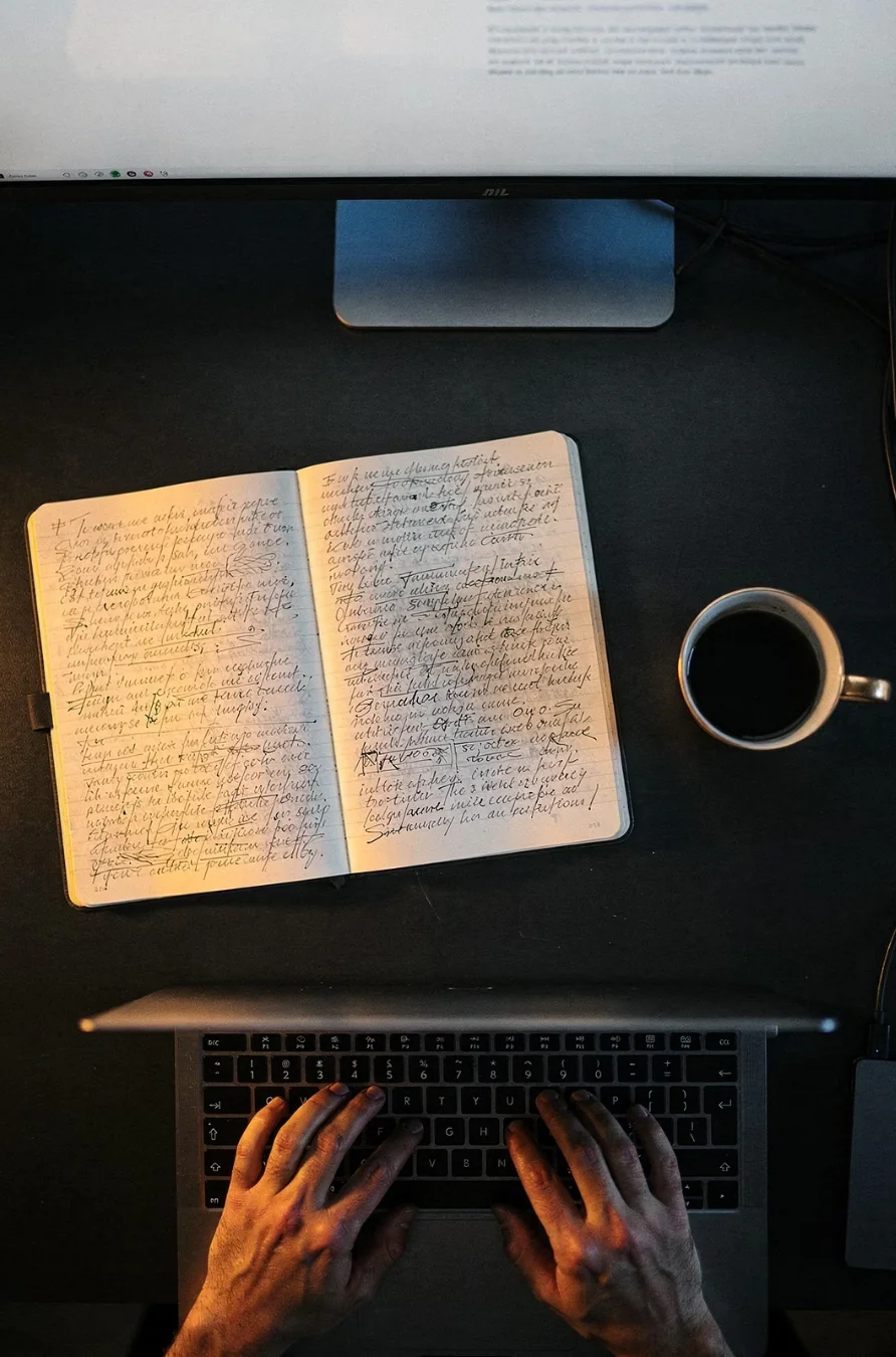 Business owner rewriting the same notes in a notebook beside a laptop and coffee, the daily re-explaining a Claude Project removes
