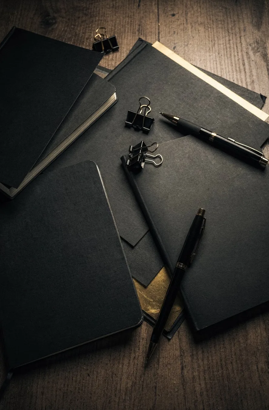 Black notebooks and pens scattered on a wooden desk, the analog version of scattered notes