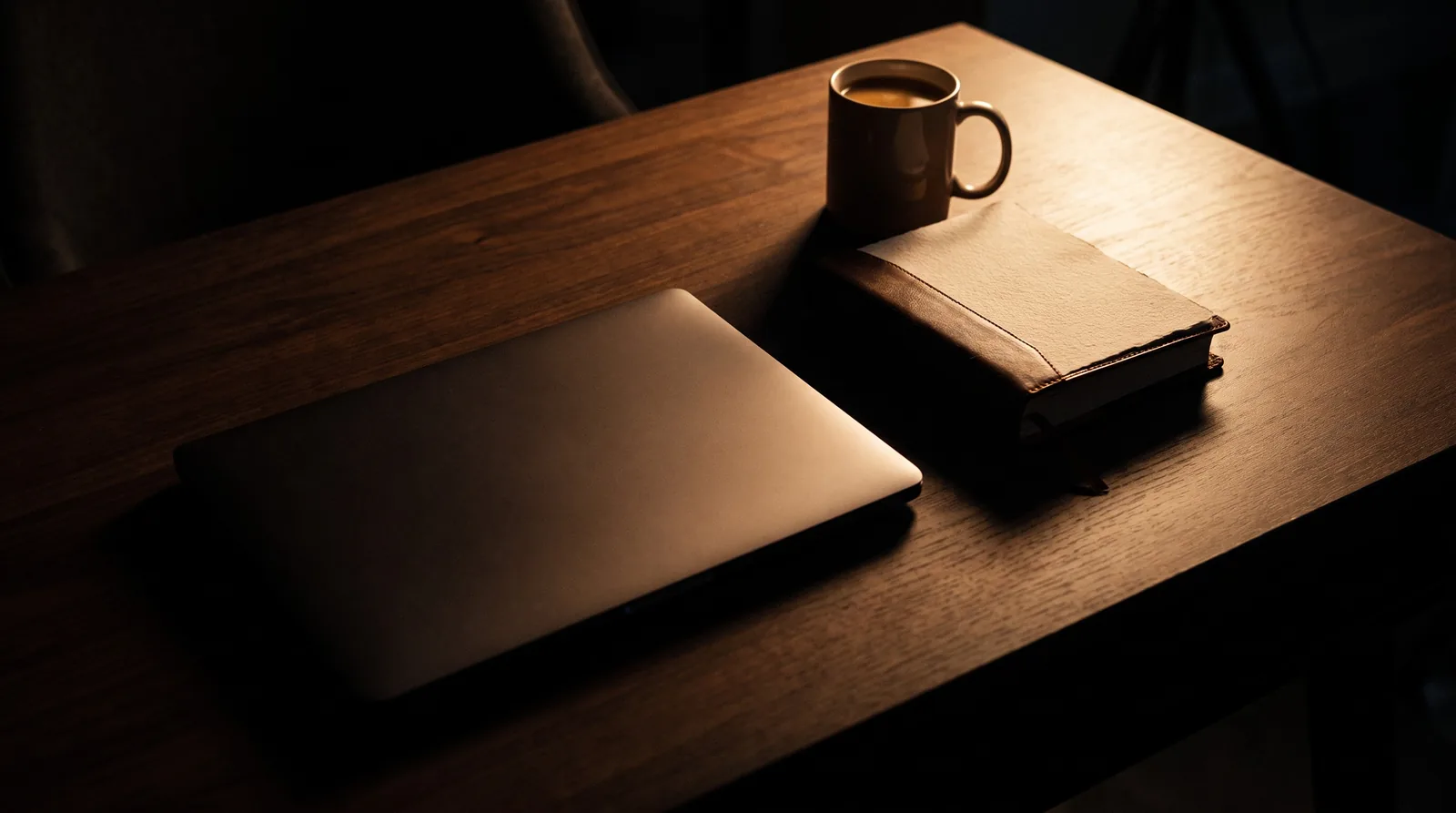 A wide overhead view of a dark desk with laptop, notebook and coffee, no text